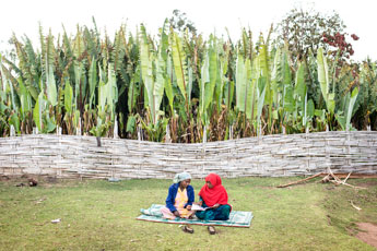 Two women sit together reading a book.